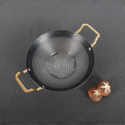 Black frying pan with gold handles on a dark gray background