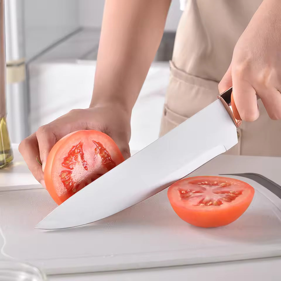 Person slicing a tomato with a large knife on a cutting board.